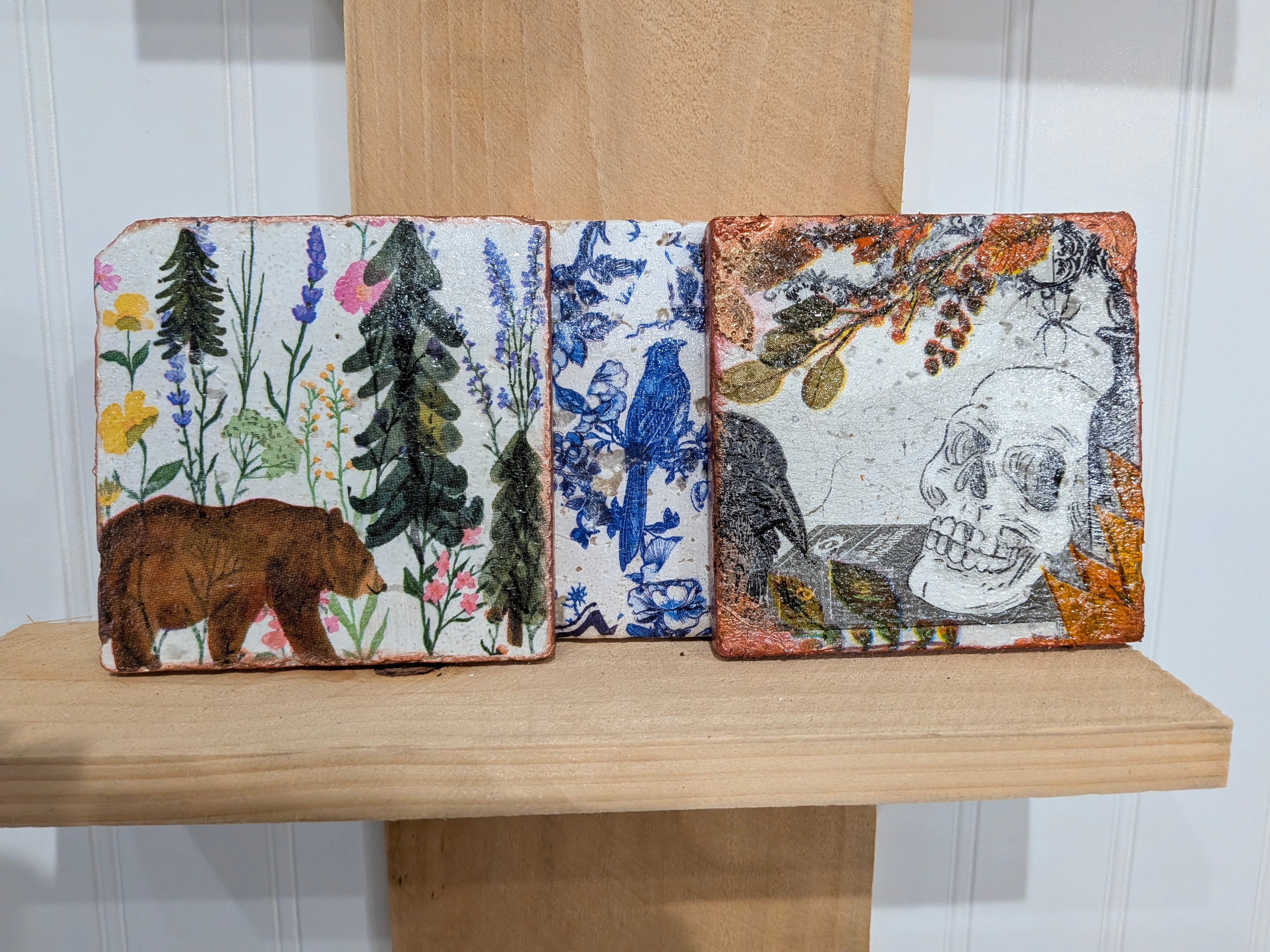Three decorative stone tiles with botanical and nature designs displayed on a shelf